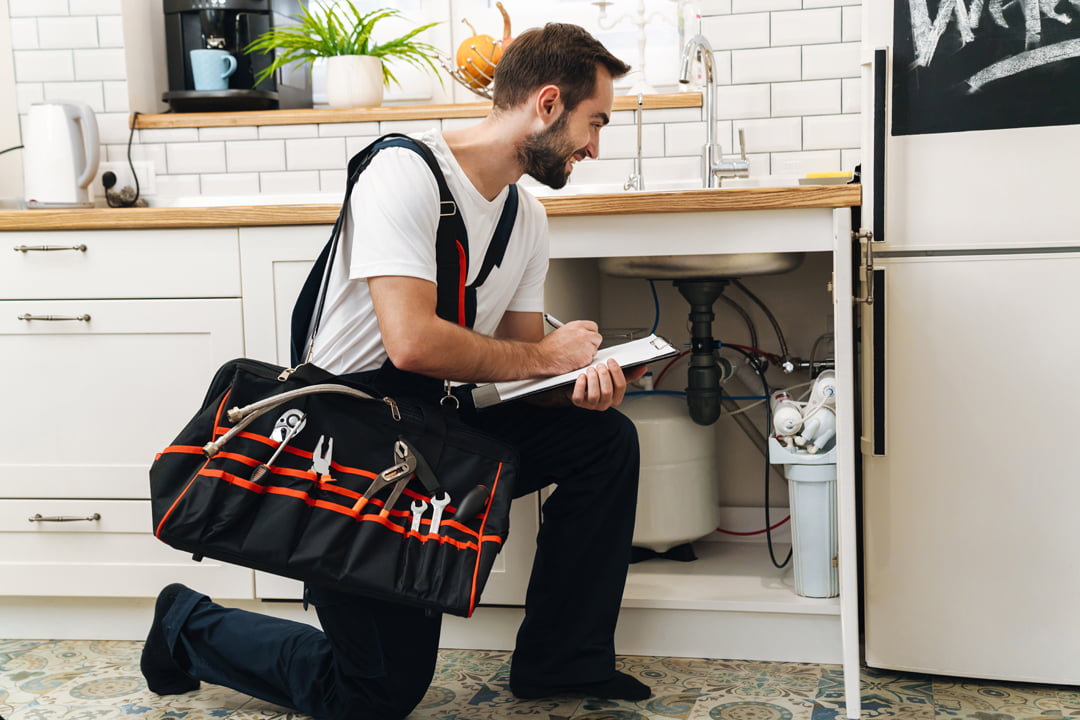 Image of young caucasian plumber man in uniform holding bag with equipment and clipboard while working in apartment
